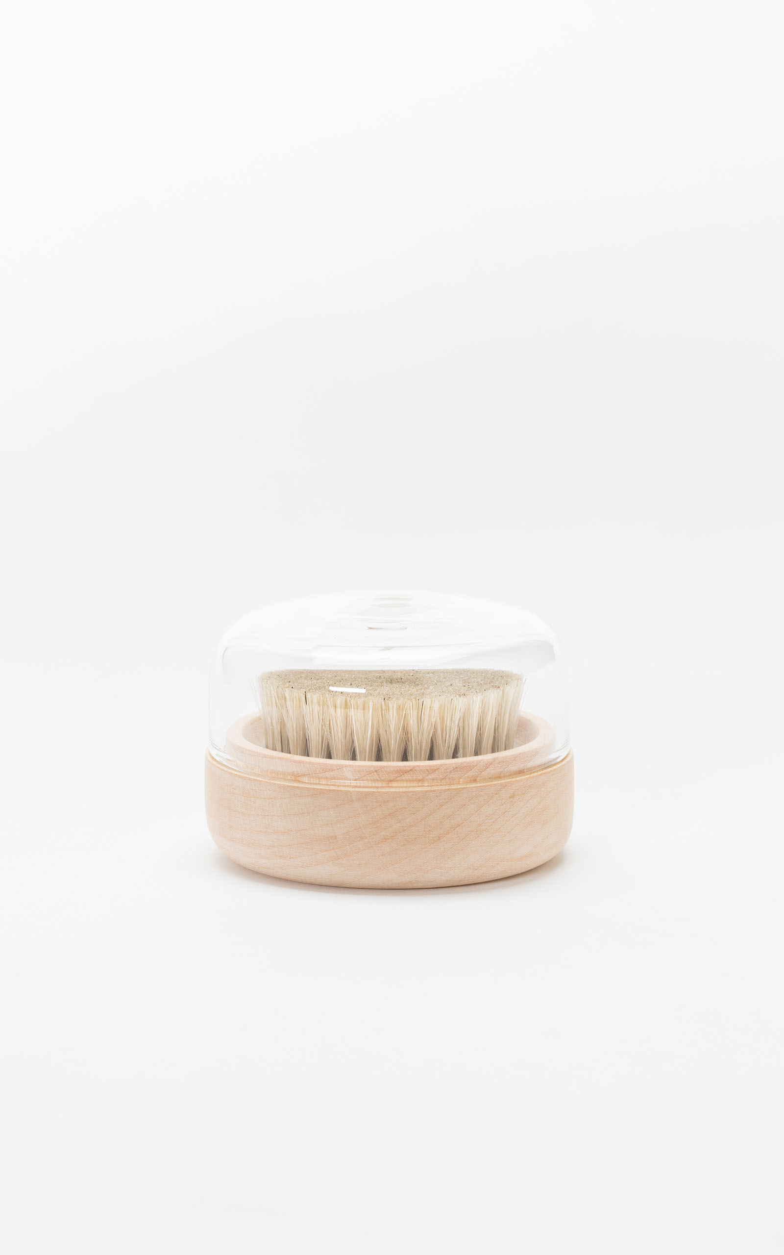 A clothing brush with a minimalistic glass top in front of a white backdrop.