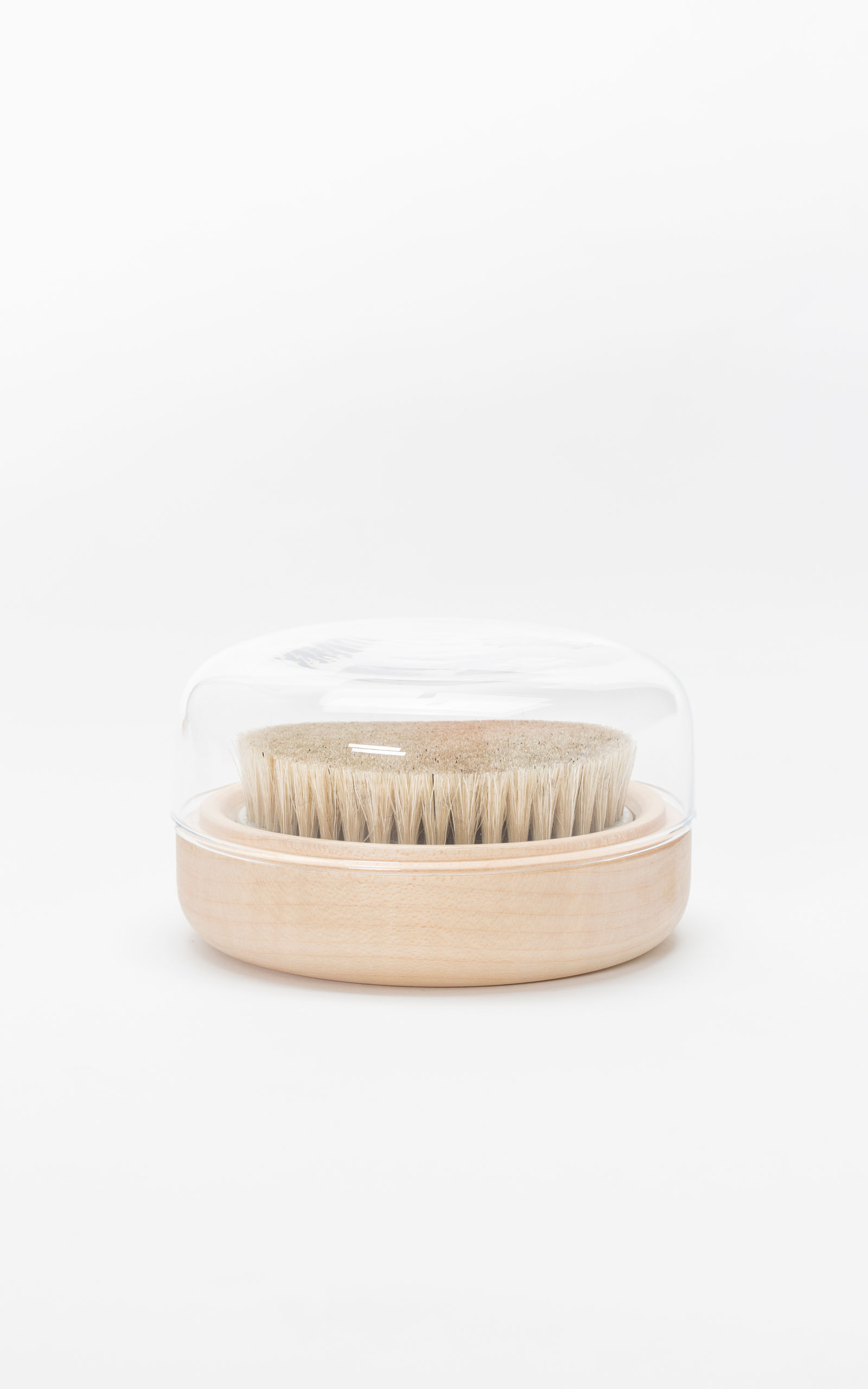A clothing brush with a minimalistic glass top in front of a white backdrop.