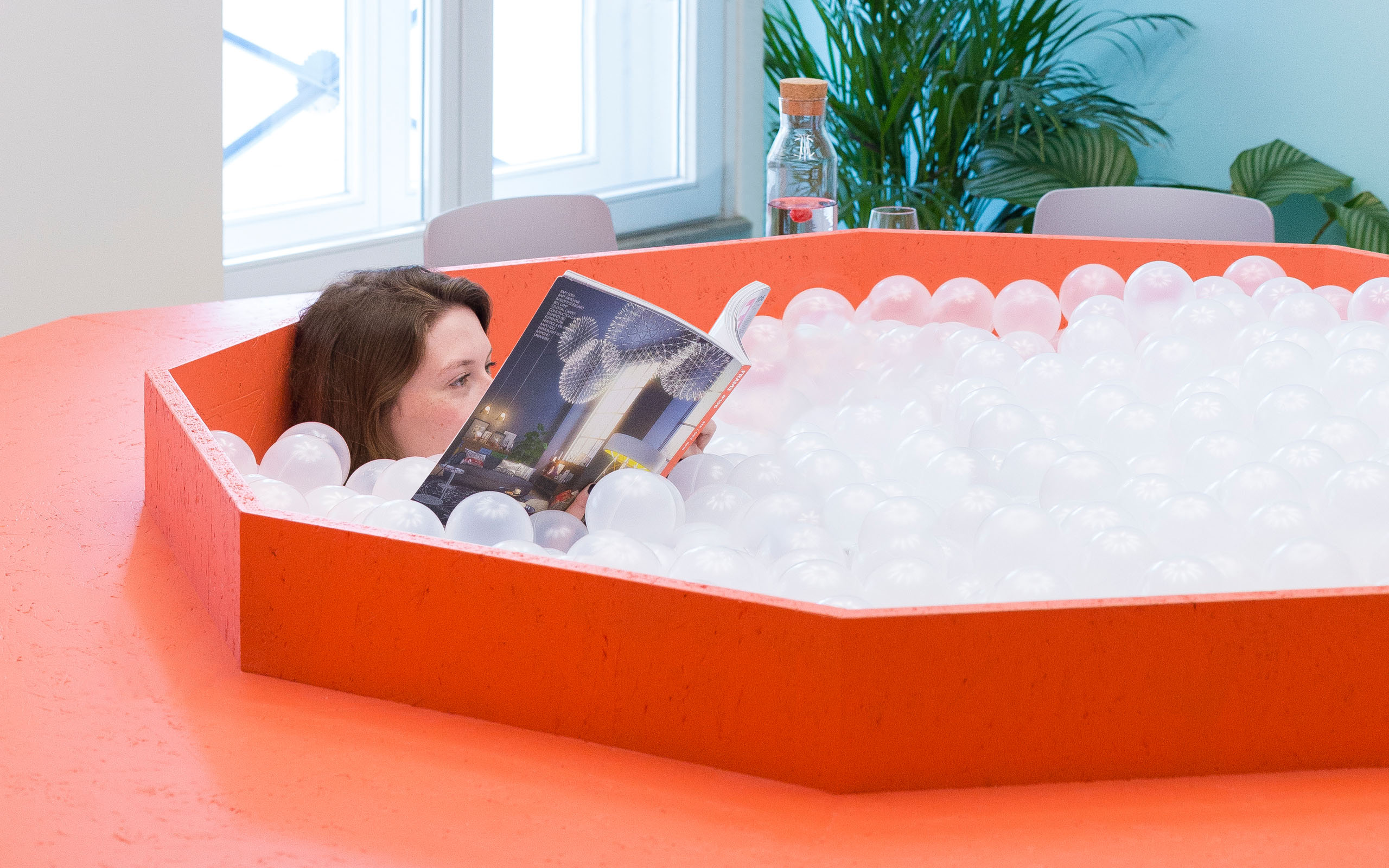 Someone is sitting in a ball pool in the Neue Denkerei which is integrated in a bright orange desk.